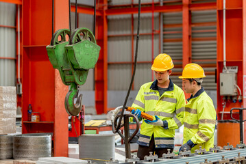 Two construction workers in yellow safety helmets and reflective vests discussing plans and safety measures at a construction site with heavy lifting equipment and steel structures © BESTIMAGE