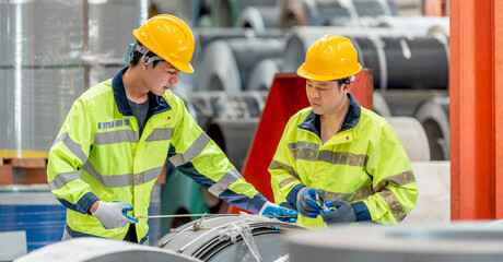 Two male construction workers wea yellow safety helmets and high-visibility jackets inspecting equipment and discussing at an industrial construction site outdoors du daytime