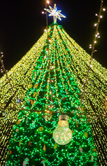 Bright christmas tree lights with glowing bulb in foreground and star on top creating magical festive holiday mood at night