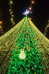 Bright christmas tree lights with glowing bulb in foreground and star on top creating magical festive holiday mood at night