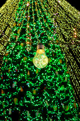 Bright christmas tree lights with glowing bulb in foreground and star on top creating magical festive holiday mood at night