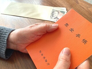 Senior holding pension booklet and cash on wooden table