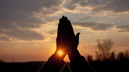 Hands in prayer against a sunset sky.