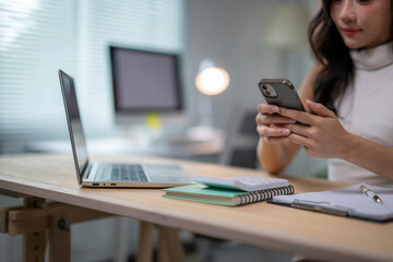 Businesswoman using smartphone and working on laptop in office