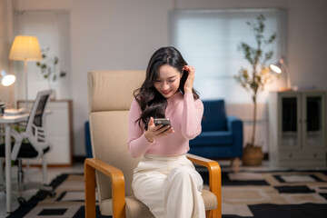 Young asian businesswoman using smartphone at home office sitting on armchair