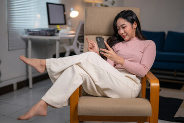 Young woman relaxing on armchair using smartphone at home