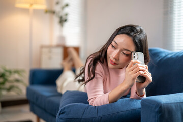 Young woman relaxing on sofa and using smartphone