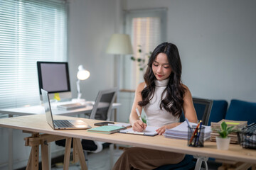 Asian businesswoman working and writing on notebook at home office