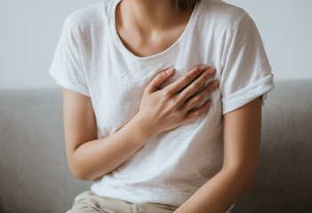 Young woman holding her chest in pain while sitting on a sofa at home, suffering from symptoms of heart attack or anxiety for medical and healthcare concepts