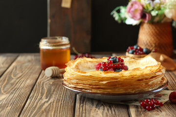 Freshly made crepes with berries and honey on a wooden table in a cozy kitchen setting during daylight hours