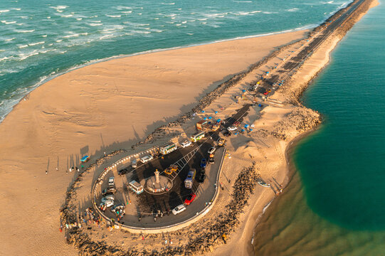 Aerial view of the tip of land meeting the sea with vehicles parked near a monument, where the golden sand contrasts with the turquoise waters, Dhanushkodi, Tamil Nadu, India.