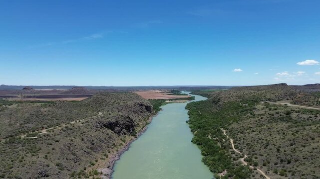 Orange River snaking through a semi-arid landscape, the camera moves lower to reveal a concrete bridge over the river. 4K Aerial Video.