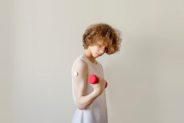 Teenage Boy with Glucose Monitor Training with Red Dumbbell on Grey Background. Authentic Concept of Diabetes Management, Active Lifestyle with Chronic Conditions, and Health Technology for Gen Z