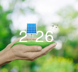 2026 white text with solar cell on green grass field in hands over blur forest, Happy new year 2026 ecological cover concept