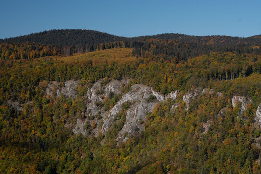 Aerial view of a dramatic cliff face amidst a sea of autumnal trees, with dark forests painting the hilltops, Ciganka, Banska Bystrica Region, Slovakia.