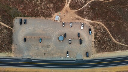 Aerial view of cars parked at a desert rest stop near a highway, the landscape a tapestry of earthy browns and muted greens, Fruita, Colorado, United States.