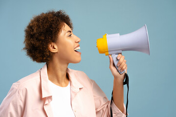 Smiling African American woman holding megaphone sharing announcement isolated on blue background