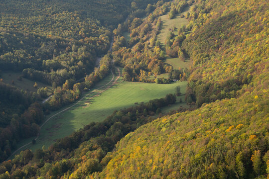 Aerial view of a vibrant green meadow nestled among the colorful autumn trees in a valley, Muranska Planina, Banska Bystrica Region, Slovakia.
