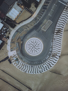 Aerial view of a roundabout with a compass rose design, surrounded by a patterned border, contrasting with the sandy terrain, Foz do Arelho, Leiria District, Portugal.