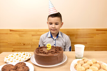 Boy seriously looking at cake with number nine candle, calm moment of celebrating a ninth birthday