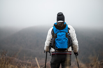 Rear view of hiker in warm clothing with backpack and hiking poles enjoying the atmospheric winter...
