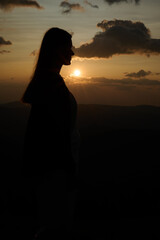 Close-up silhouette of a young woman standing on a mountain at sunrise. Peaceful morning in nature, thoughtful expression, natural beauty and golden light.