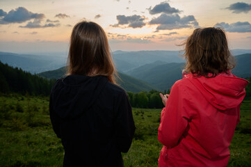 Two girls hikers in the mountains. Back view. Peaceful outdoor moment, reconnecting with nature and mindfulness practice in a scenic setting. Slim, sporty women standing against vivid landscape.