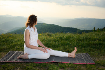 Woman sitting on a yoga mat in the mountains, meditating at sunrise. Peaceful outdoor moment, reconnecting with nature and mindfulness practice in a scenic setting.