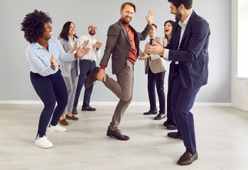 Man joyfully dancing surrounded by applauding team of colleagues, celebrating success during a...