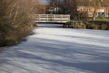 Wooden footbridge over frozen pond in winter park landscape