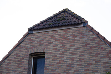 Detail of red brick house gable with tiled roof edge and moss