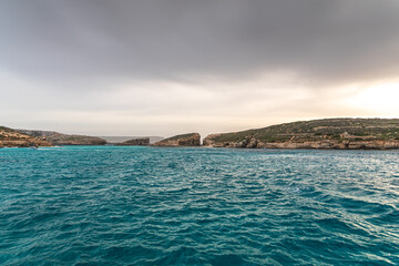 Malta Blue Lagoon landscape. Stunning view of the Blue Lagoon in Comino, Malta, showing the famous turquoise crystal clear waters and the rocky islet of Cominotto under a cloudy sky.