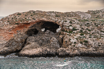 Malta Blue Lagoon landscape. Stunning view of the Blue Lagoon in Comino, Malta, showing the famous turquoise crystal clear waters and the rocky islet of Cominotto under a cloudy sky.