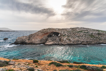 Malta Blue Lagoon landscape. Stunning view of the Blue Lagoon in Comino, Malta, showing the famous turquoise crystal clear waters and the rocky islet of Cominotto under a cloudy sky.
