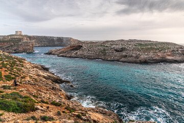 Malta Blue Lagoon landscape. Stunning view of the Blue Lagoon in Comino, Malta, showing the famous turquoise crystal clear waters and the rocky islet of Cominotto under a cloudy sky.