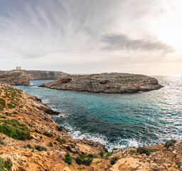 Malta Blue Lagoon landscape. Stunning view of the Blue Lagoon in Comino, Malta, showing the famous turquoise crystal clear waters and the rocky islet of Cominotto under a cloudy sky.