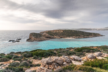 Malta Blue Lagoon landscape. Stunning view of the Blue Lagoon in Comino, Malta, showing the famous turquoise crystal clear waters and the rocky islet of Cominotto under a cloudy sky.