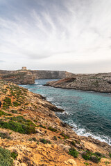 Malta Blue Lagoon landscape. Stunning view of the Blue Lagoon in Comino, Malta, showing the famous turquoise crystal clear waters and the rocky islet of Cominotto under a cloudy sky.