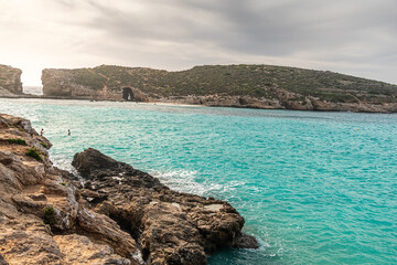 Malta Blue Lagoon landscape. Stunning view of the Blue Lagoon in Comino, Malta, showing the famous turquoise crystal clear waters and the rocky islet of Cominotto under a cloudy sky.