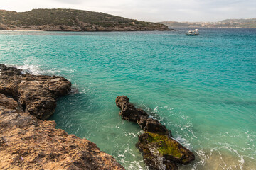 Malta Blue Lagoon landscape. Stunning view of the Blue Lagoon in Comino, Malta, showing the famous turquoise crystal clear waters and the rocky islet of Cominotto under a cloudy sky.