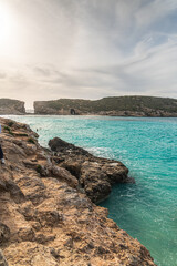 Malta Blue Lagoon landscape. Stunning view of the Blue Lagoon in Comino, Malta, showing the famous turquoise crystal clear waters and the rocky islet of Cominotto under a cloudy sky.