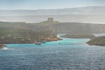 High-angle view of the famous Blue Lagoon in Comino, Malta, featuring crystal clear turquoise waters, tour boats, and the rugged coastline of the small island.