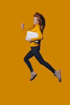 Woman wearing denim and sweater enthusiastically jumps holding computer