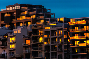 Beautiful twilight view of Balluta Bay in St. Julians, Malta, featuring the illuminated neo-gothic Parish Church of Our Lady of Mount Carmel and pink sunset clouds.