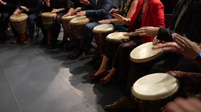 Group of individuals rhythmically playing hand drums in a seated circle, showcasing synchronized movements and vibrant energy, hands in motion creating a lively musical atmosphere