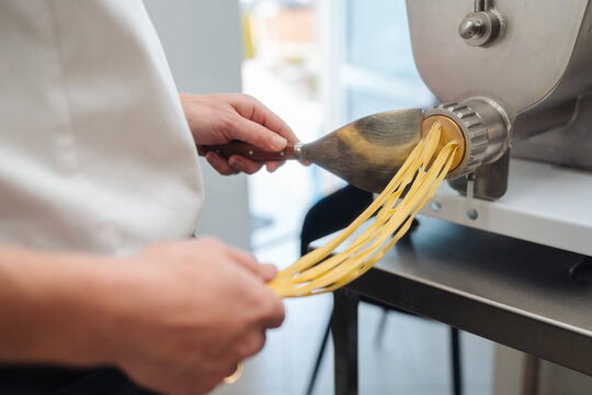 Closeup of hands guiding dough through industrial pasta cutter