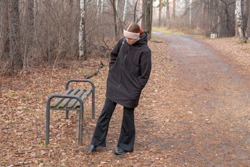 Young girl standing on a bench with autumn foliage around in a park, enjoying the fall season. Autumn walk and relaxation.