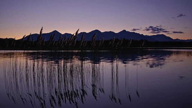 purple twilight over mountain lake reeds reflecting mirror image calm water and silhouetted ridge under gradient indigo sky, delicate clouds, meditative atmosphere, ideal for travel editorial,