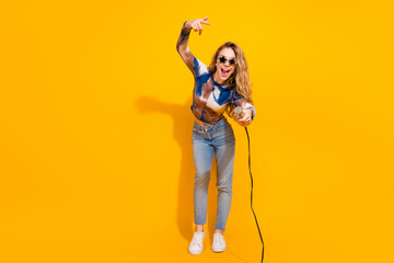 Young woman sings into microphone against bright yellow background during lively casual fashion shoot