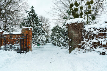 An open gate with a cross towards a snow-covered park with trees, Chelm, Poland